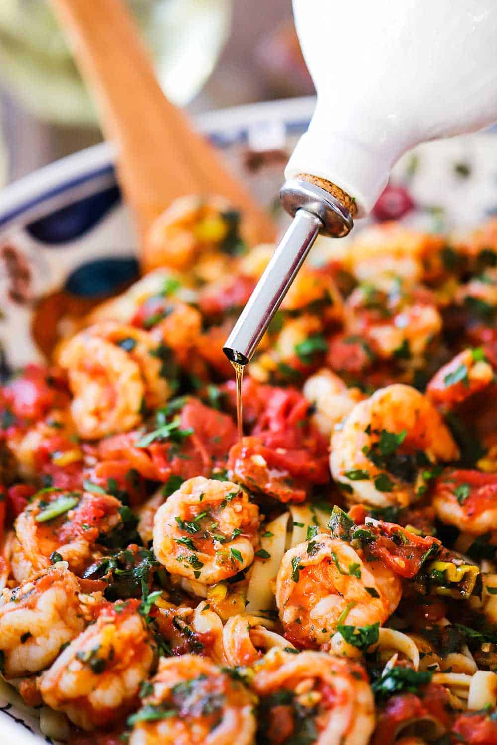 A white olive oil bottle pouring olive oil over a pasta bowl filled with shrimp fra diavolo.