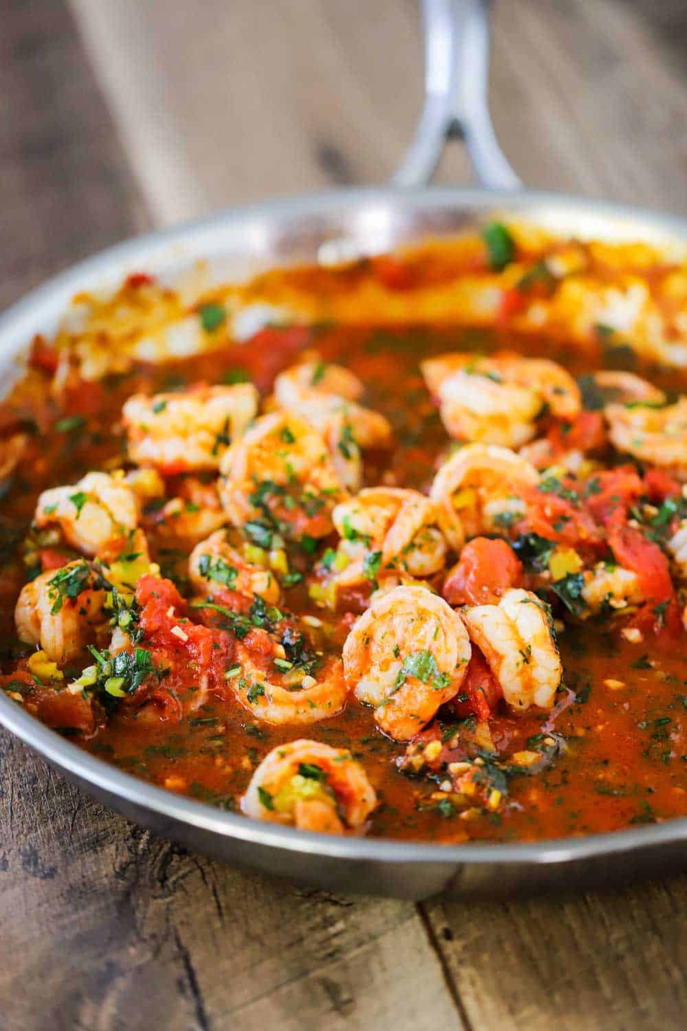 A large silver skillet filled with cooked shrimp fra diavolo sitting on wooden planks.