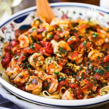 A large festive pasta bowl filled with shrimp fra diavolo with sliced Italian bread next to it and a glass of white wine.
