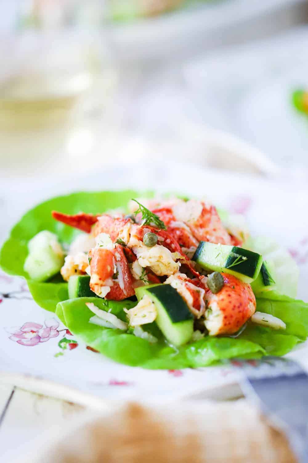A close-up view of a lobster salad with cucumbers on a green leaf of lettuce on a decorative plate.