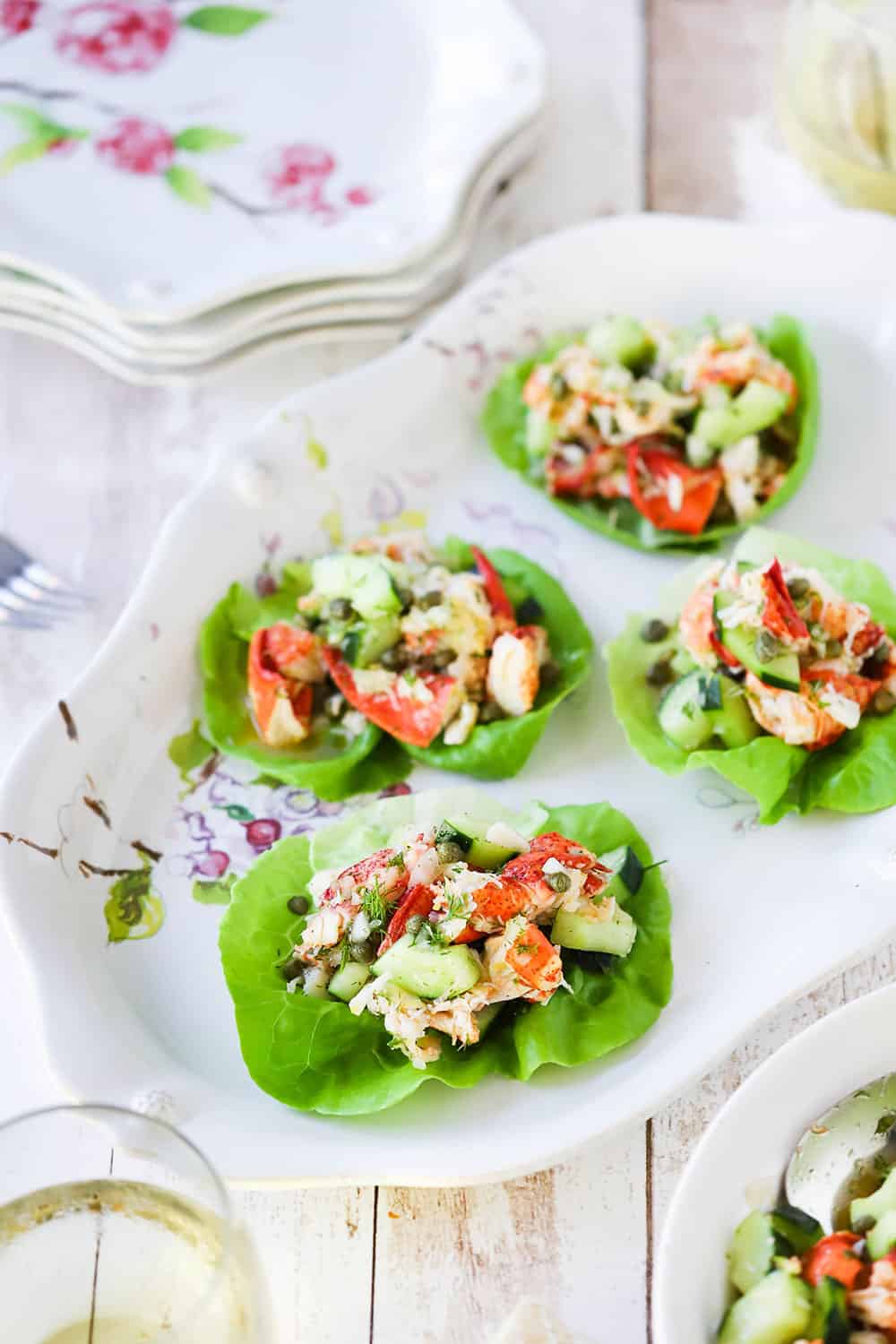 A large decorative platter filled with 4 lettuce leafs topped with a lobster salad with cucumbers and herbs.