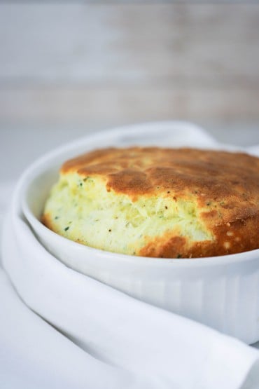 A white large dish filled with a cheese souffle with asparagus with a white napkin next to it.