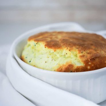 A white large dish filled with a cheese souffle with asparagus with a white napkin next to it.