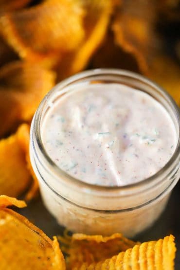 A small Mason glass jar filled with a spicy remoulade next to cross hatch sweet potato chips.