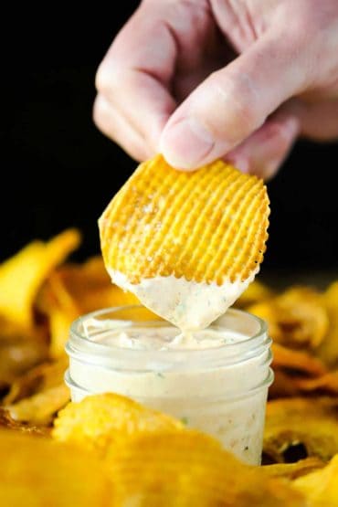 A hand dipping a cross hatch sweet potato chip into a small jar of kickin' remoulade sauce.