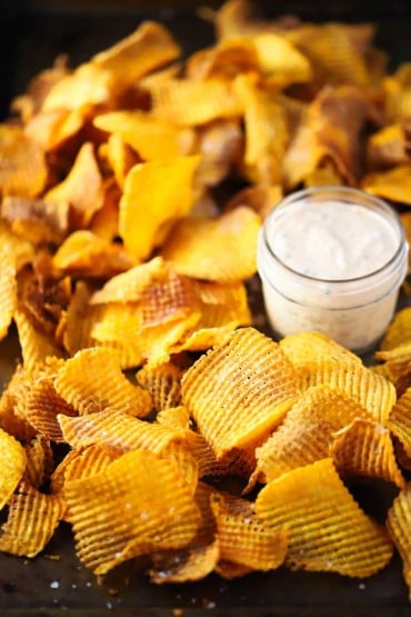 A large baking dish filled with cross hatch sweet potato chips with a small glass jar of spicy remoulade nestled into the chips.