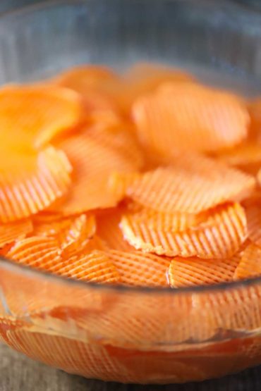 A large glass bowl filled with sliced sweet potatoes in a cross hatch style soaking in water.