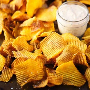 A large baking dish filled with cross hatch sweet potato chips with a small glass jar of spicy remoulade nestled into the chips.