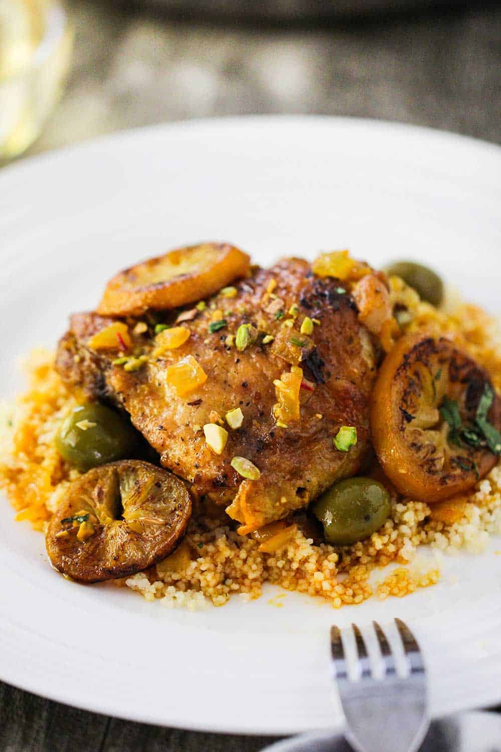 A white plate filled with chicken tagine with preserved lemons and olives with a fork resting on the plate. 