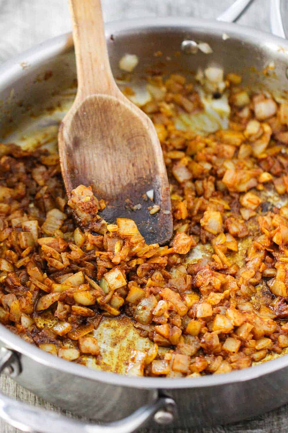 A skillet filled with sautéed onions and Moroccan spices with a wooden spoon in the middle. 