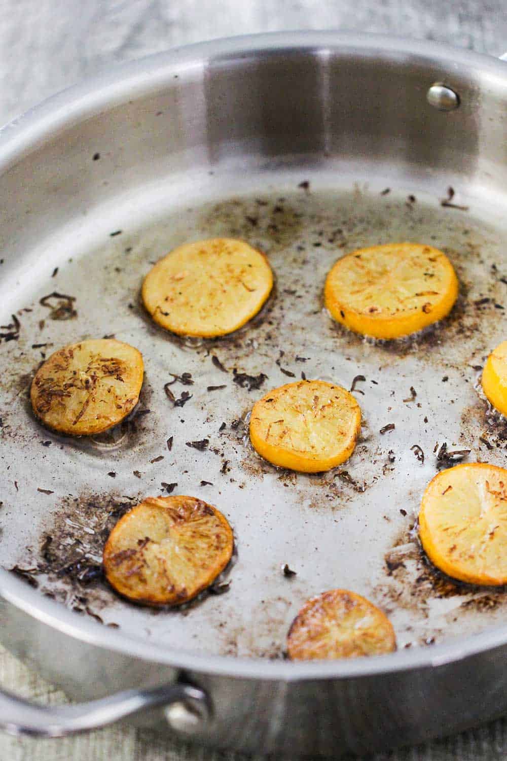 Seared slicked preserved lemons in a stainless steel skillet. 