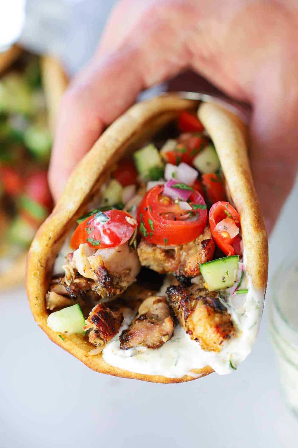 A hand holding a folded chicken gyro with tzatziki sauce inside.