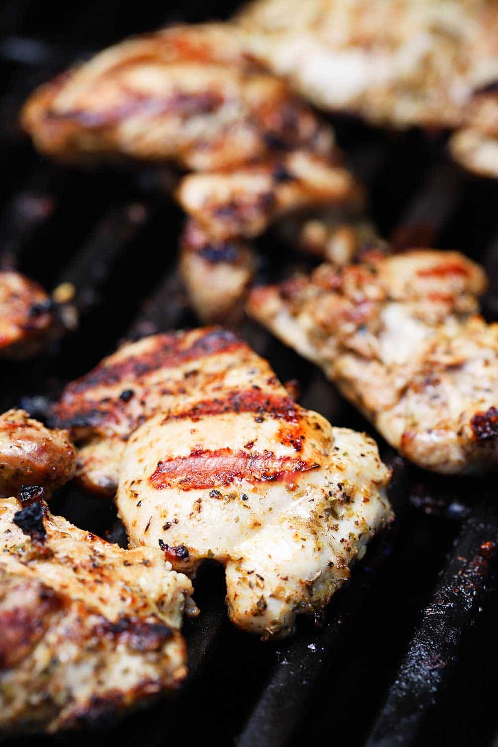 A close up view of seasoned, cooked chicken thighs on hot grill.