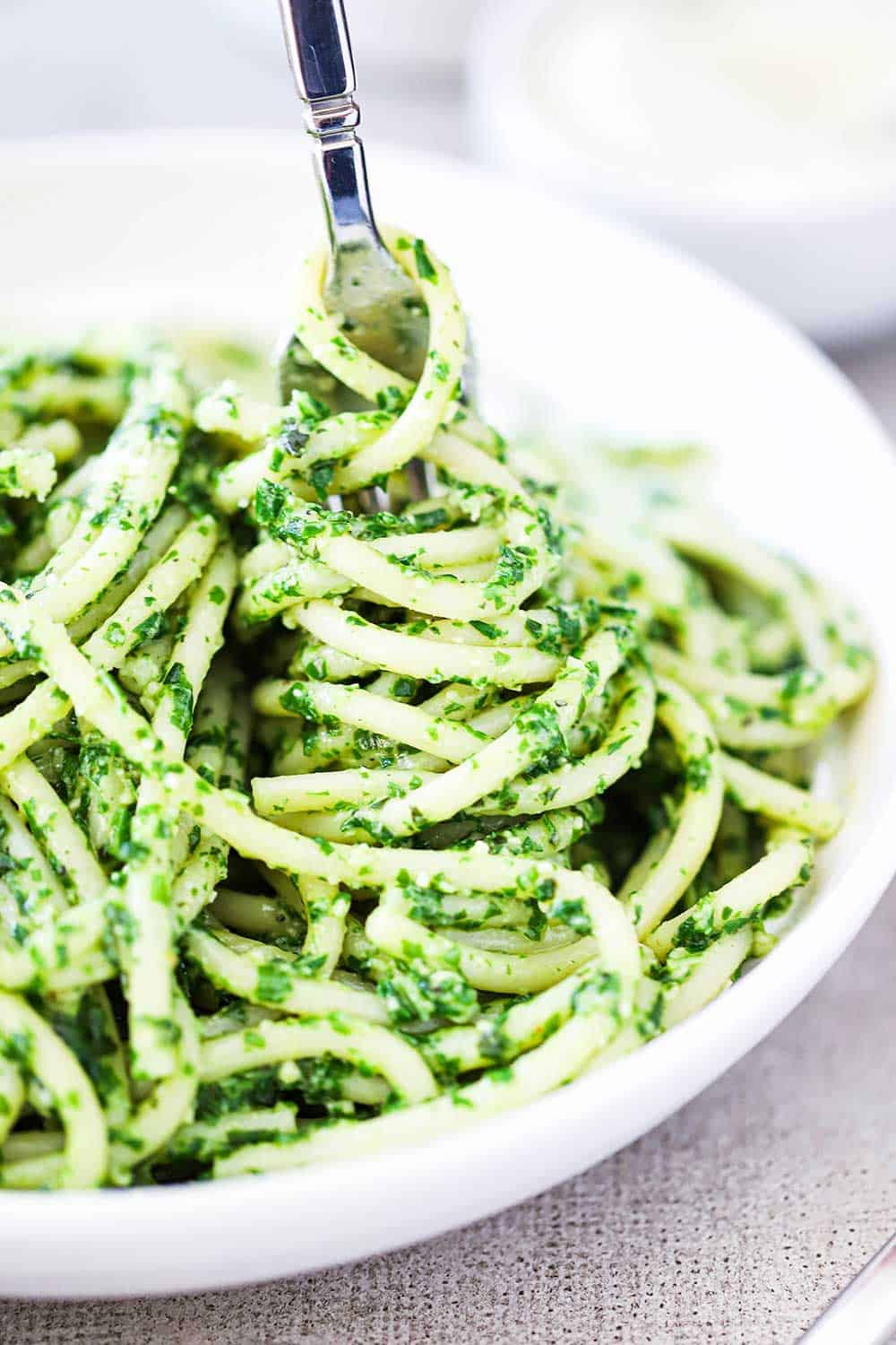 A close up view of a bowl filled with spaghetti and pesto sauce with a fork twisting the pasta.