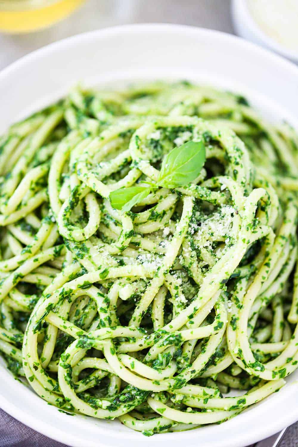 An overhead view of a white pasta bowl filled with pesto pasta with a small basil leaf on top.