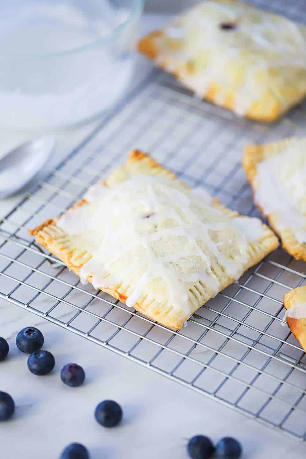 Homemade blueberry pop tarts on a baking rack with fresh blueberries and spoon sitting nearby.