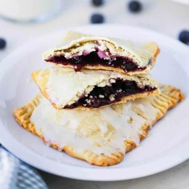 A small white plate holding 2 homemade blueberry pop tarts, one that is split open on top, sitting next to a glass of milk.