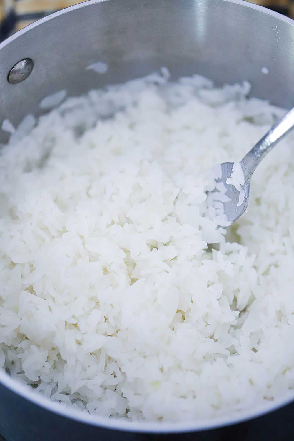 An overhead view looking down into a silver pan filled with fluffy cooked Jasmine rice with a fork in it. 