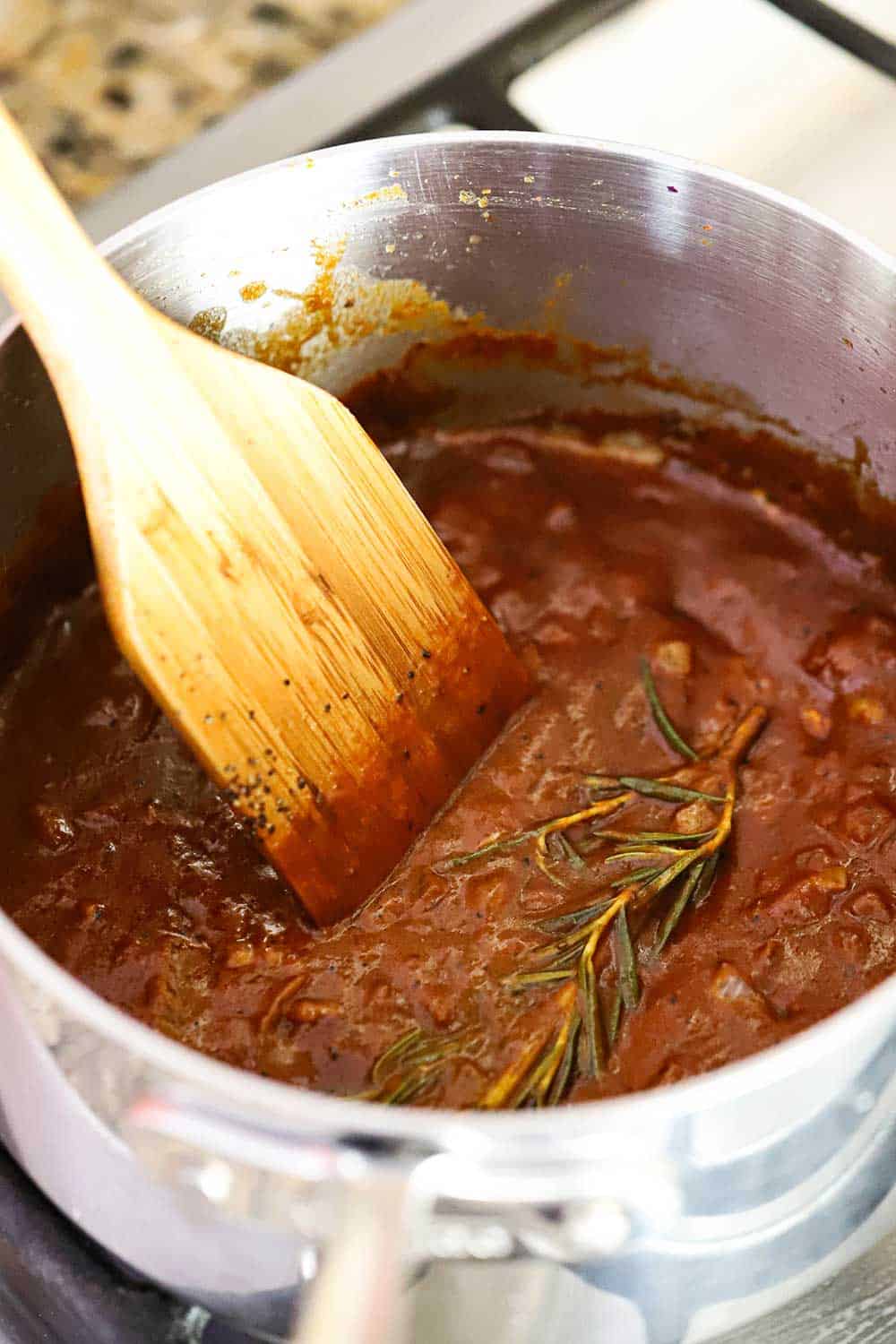 A medium-sized silver saucepan filled with homemade steak sauce with a wooden spoon in it. 