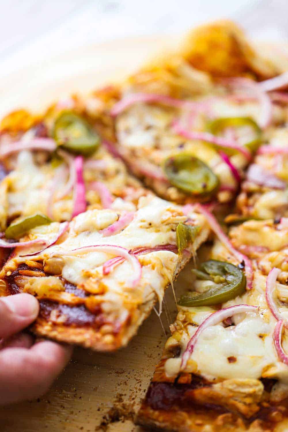 A close up view of a hand pulling a slice of thin crust BBQ chicken pizza.