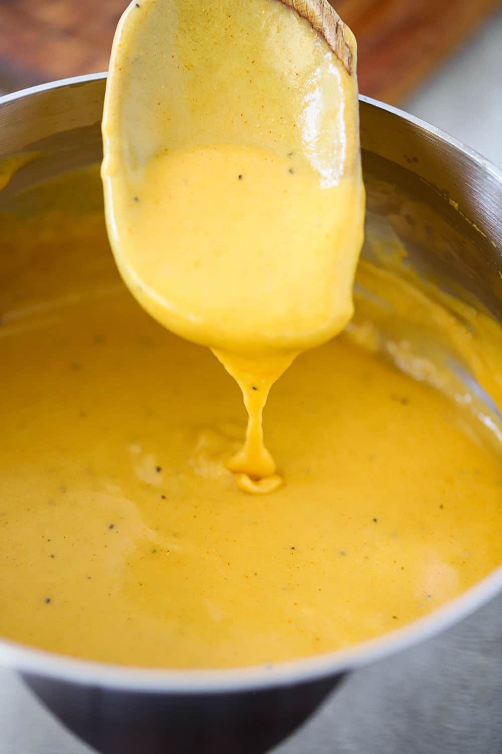 A large wooden spoon filled with beer cheese sauce in a medium saucepan. 