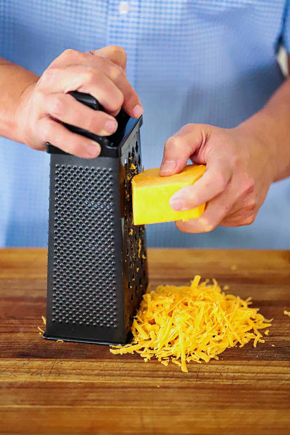 A hand shredding a block of cheddar cheese on a box grater. 