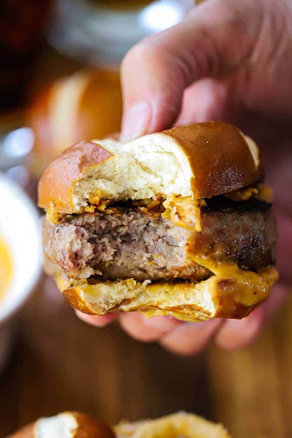 A hand holding a pretzel bratwurst sider with a bite taken out. 