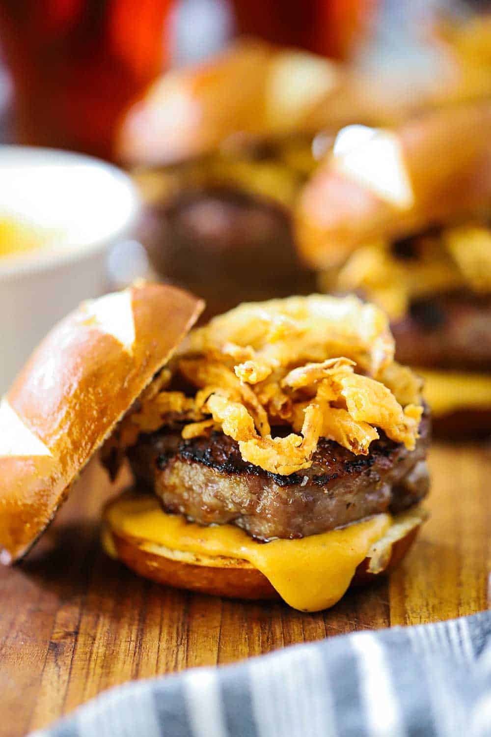 A bratwurst slider on a pretzel bun with cheese sauce and fried onions on a cutting board. 