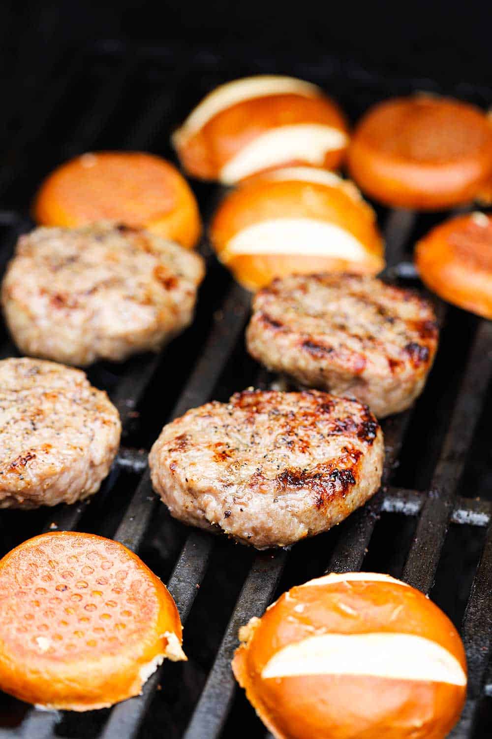 Bratwurst sliders and pretzel buns cooking on a gas grill. 