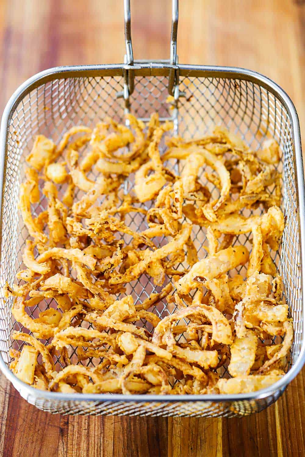 An overhead view of a deep-fryer basket filled with fried onion strips. 