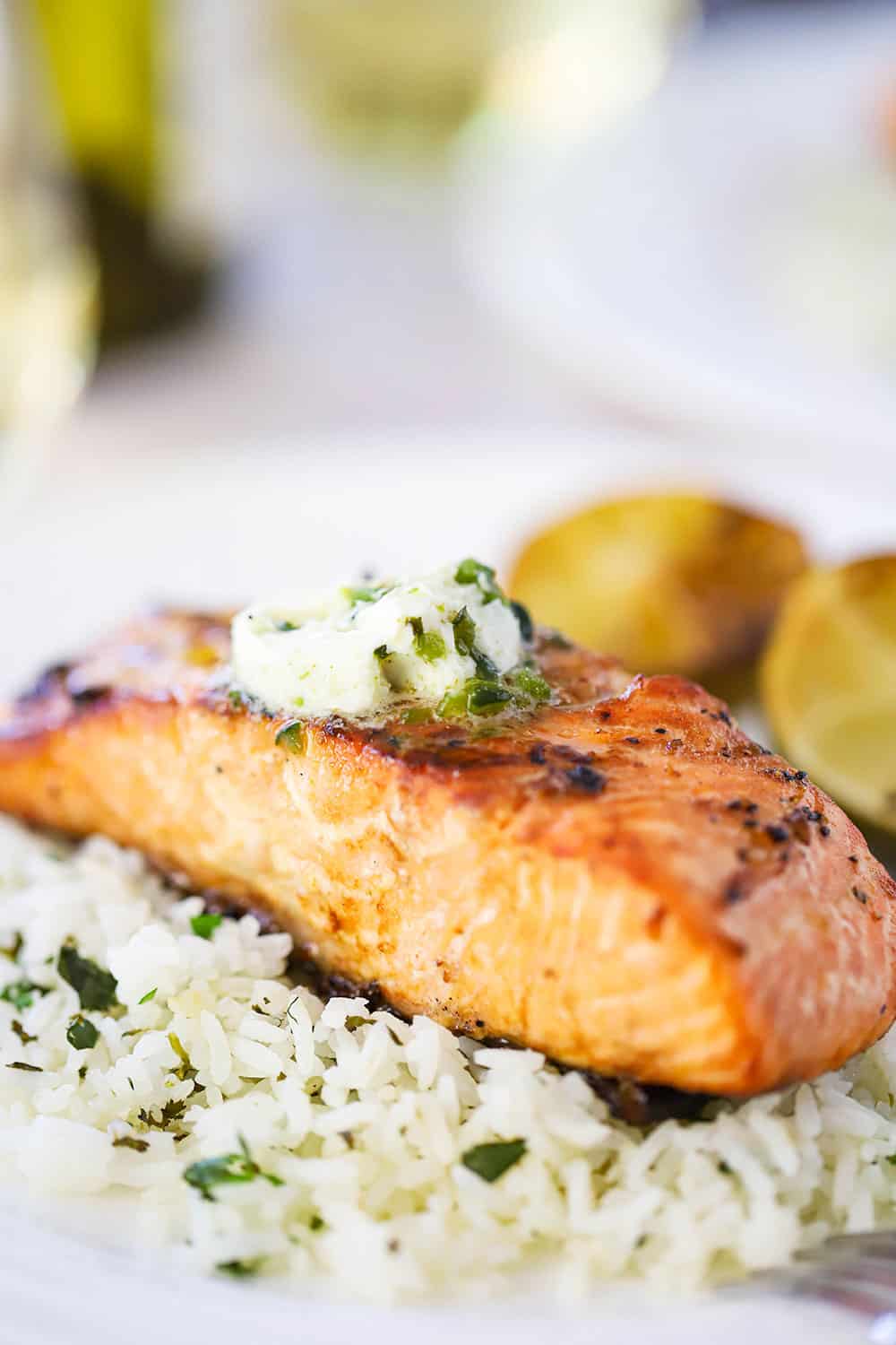 A close up view of a fillet of grilled salmon topped with a pad of melting poblano butter sitting on a bed of cilantro rice on a white plate.