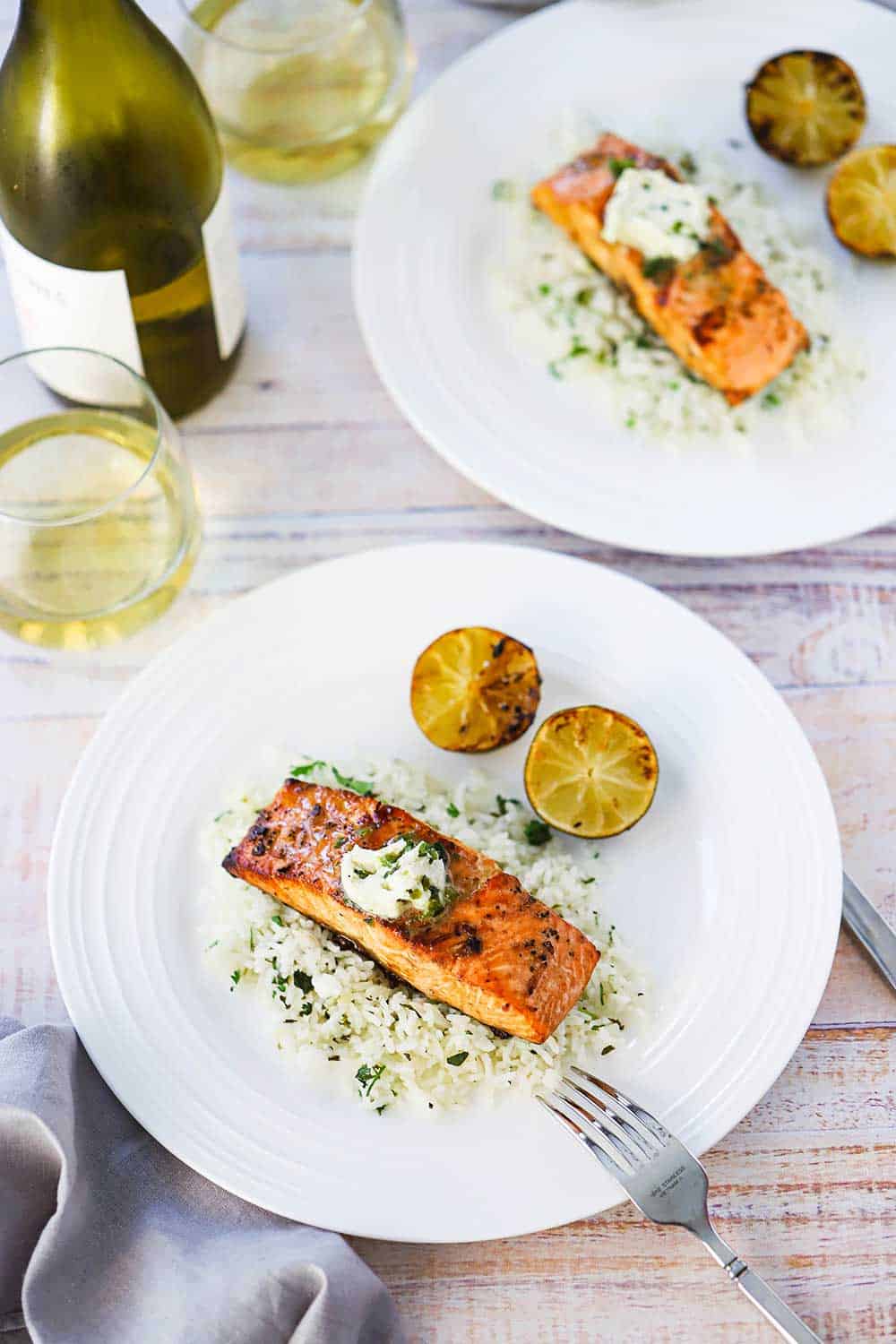 An overhead view of two white plates both holding grilled salmon with poblano butter sitting on top.