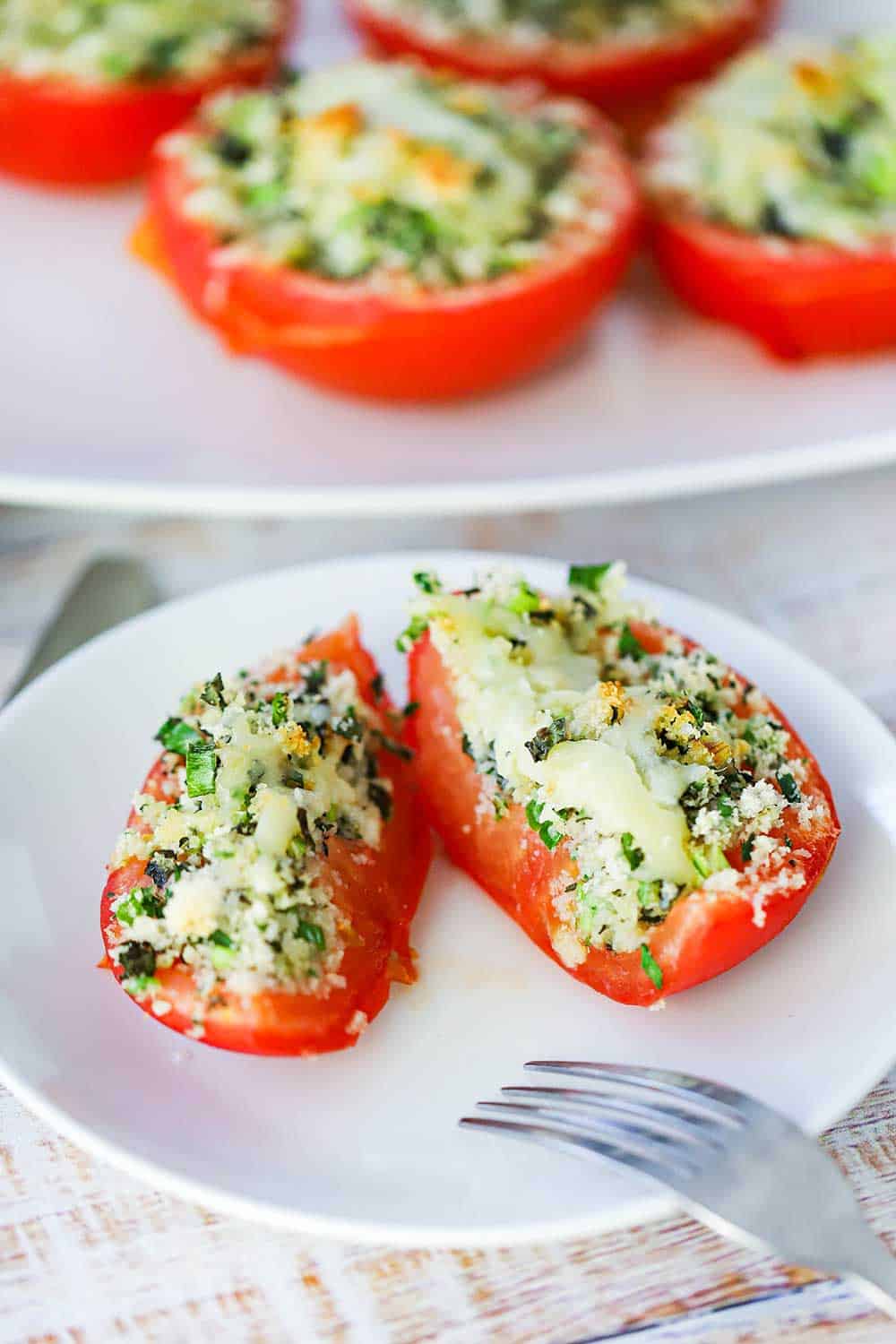 A white plate with a sliced stuffed tomato on it with a fork on the side of the plate.