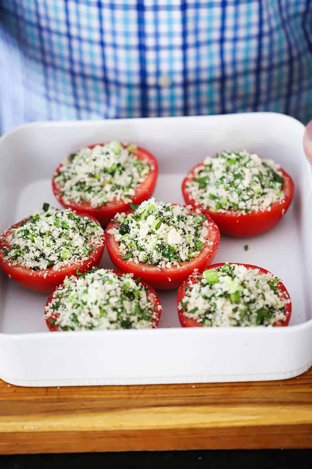 A white baking dish filled with 6 tomato halves filled with bread crumb filling in a white baking dish.