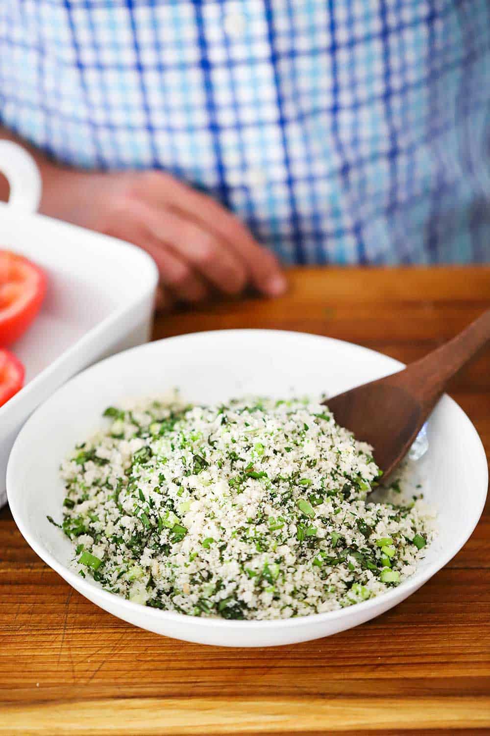 A white bowl filled with fresh bread crumbs and herbs with a wooden spoon in it.