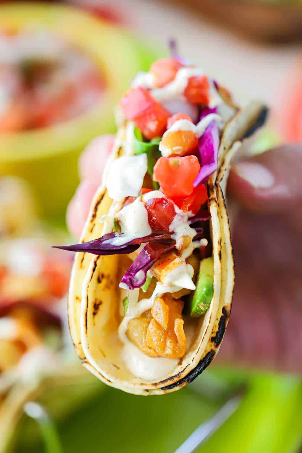 A hand holding a baja fish taco with pico de gallo topping.