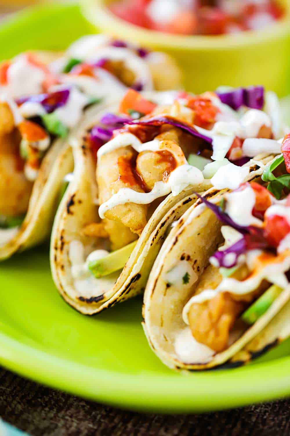 A close up view of three Baja fish tacos on a bright green platter.