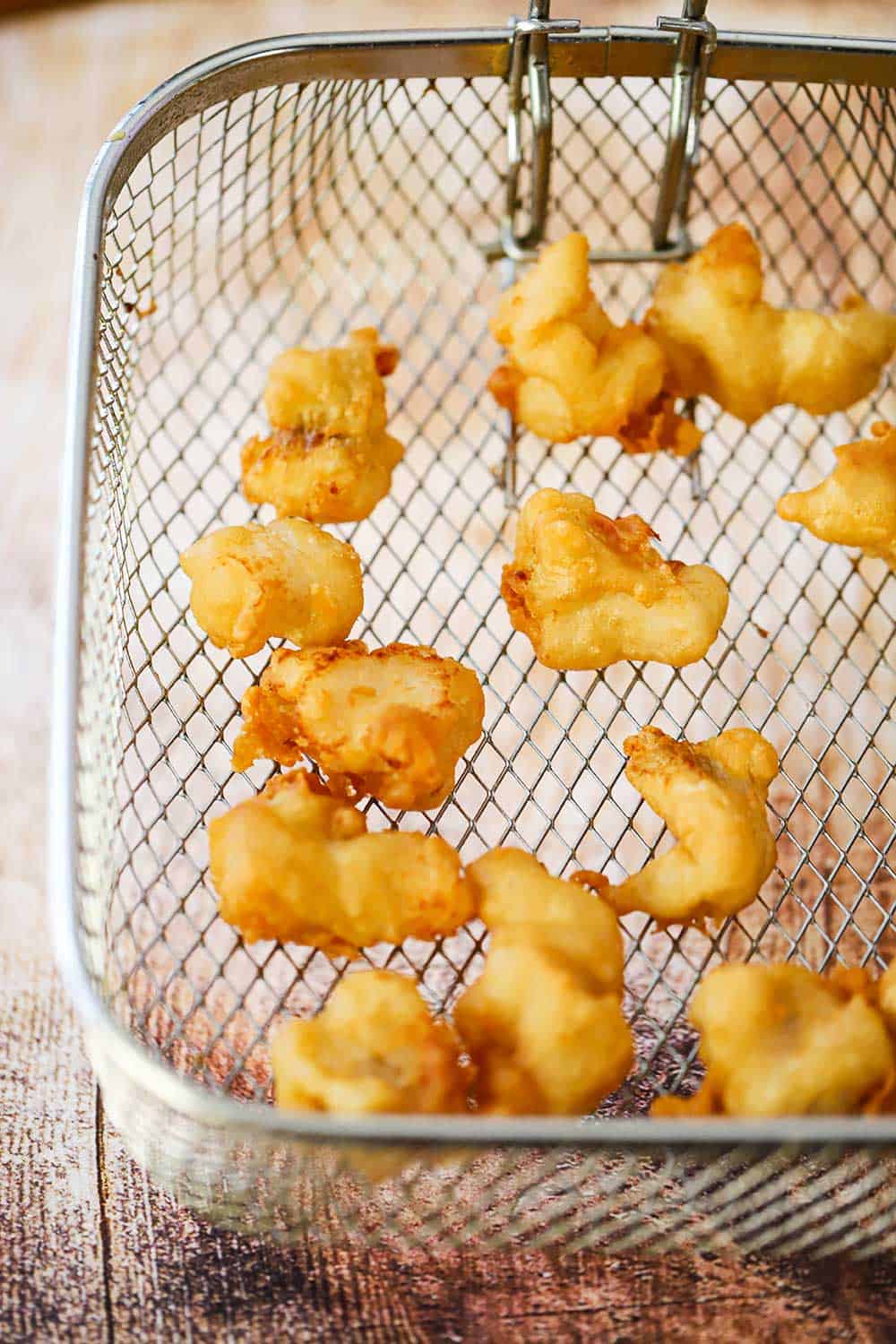 An overhead view of a deep fryer basket filled with golden pieces of fried cod