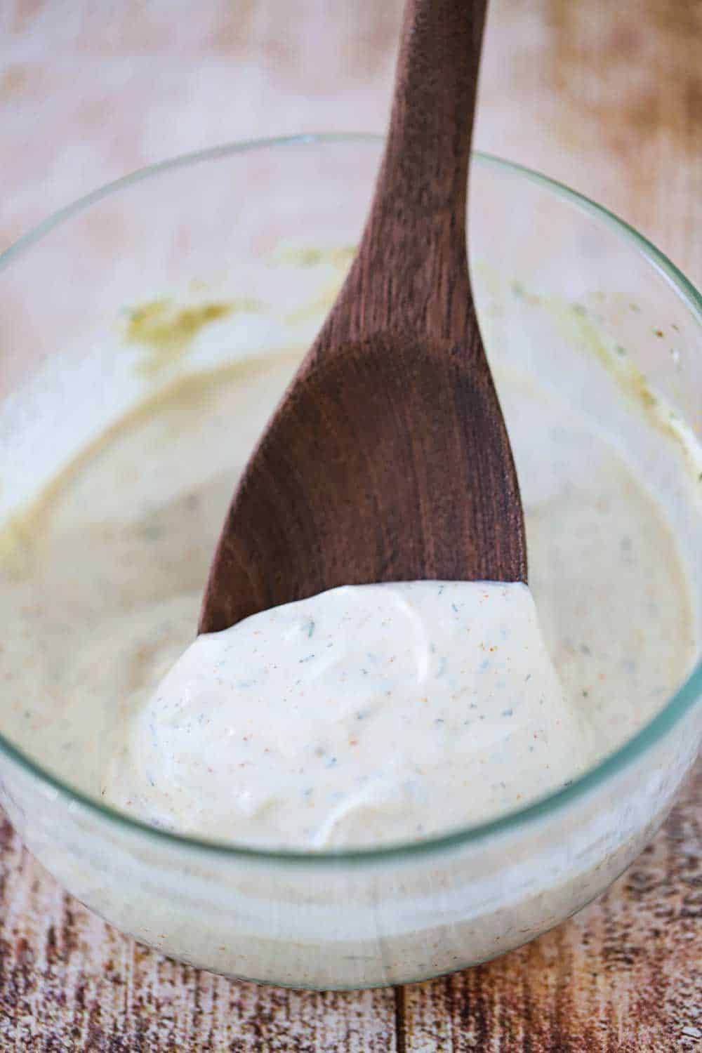 A small glass bowl filled with Baja sauce with a wooden spoon in it.