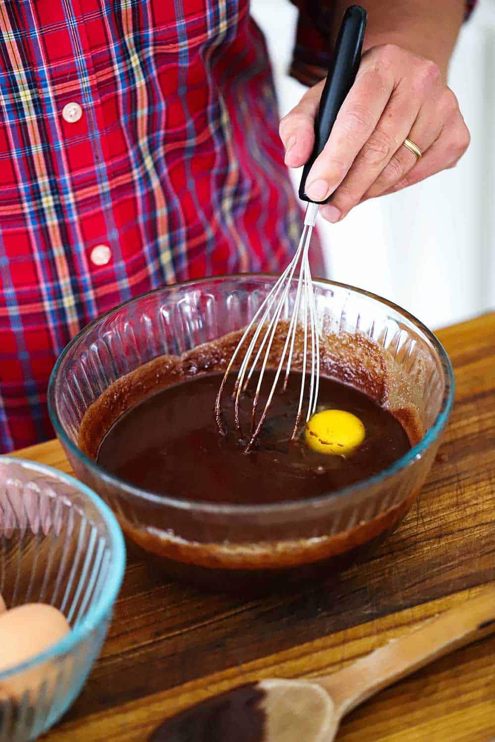 A person whisking an egg into fudge brownie batter in a glass bowl. 