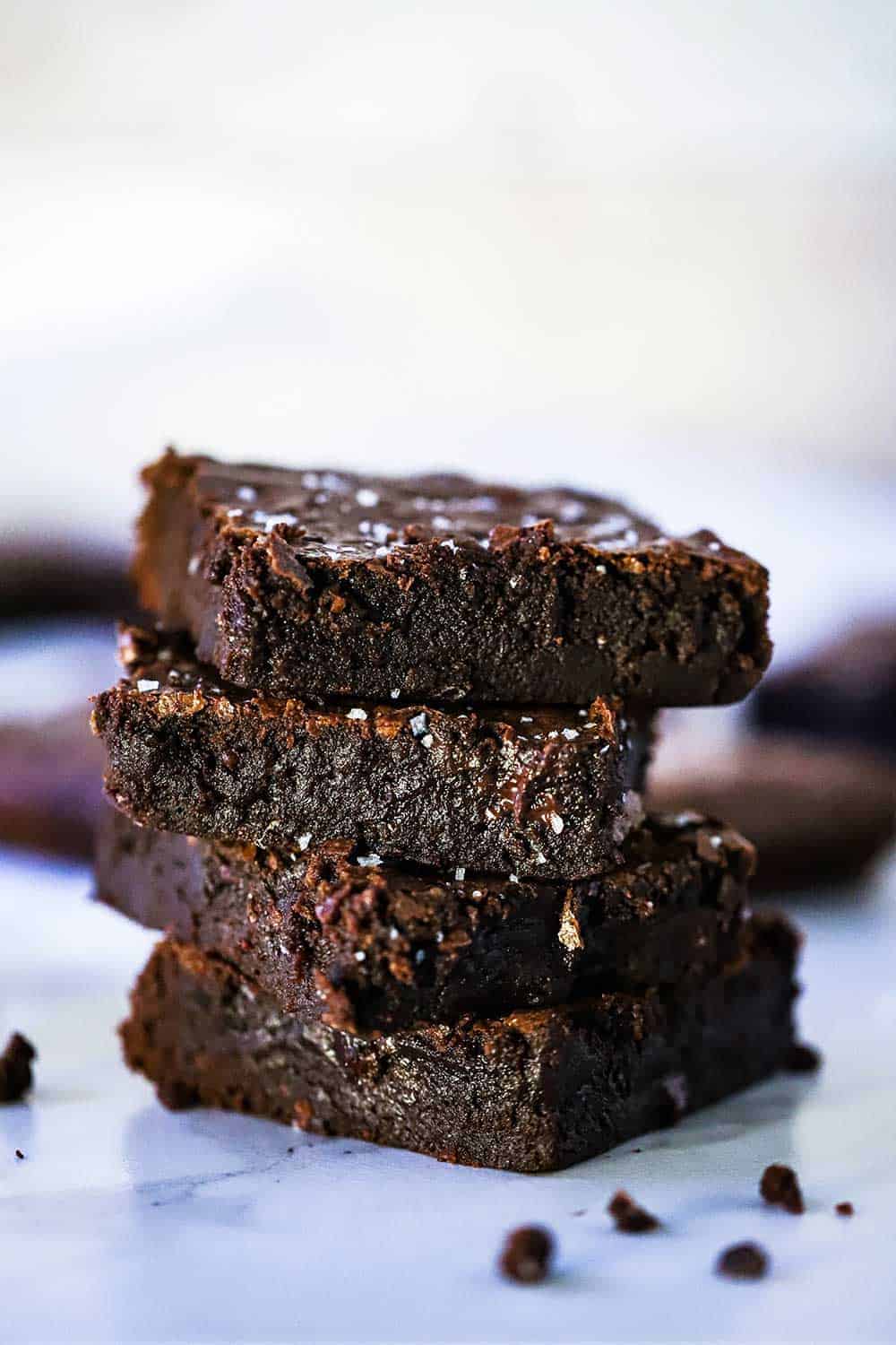 Four stacked fudge brownies on parchment paper with crumbs scattered nearby. 