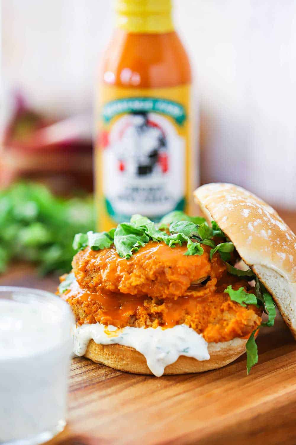 A sandwich of two chicken cutlets with buffalo wing sauce on them and sitting on blue cheese dressing and hamburger buns. 