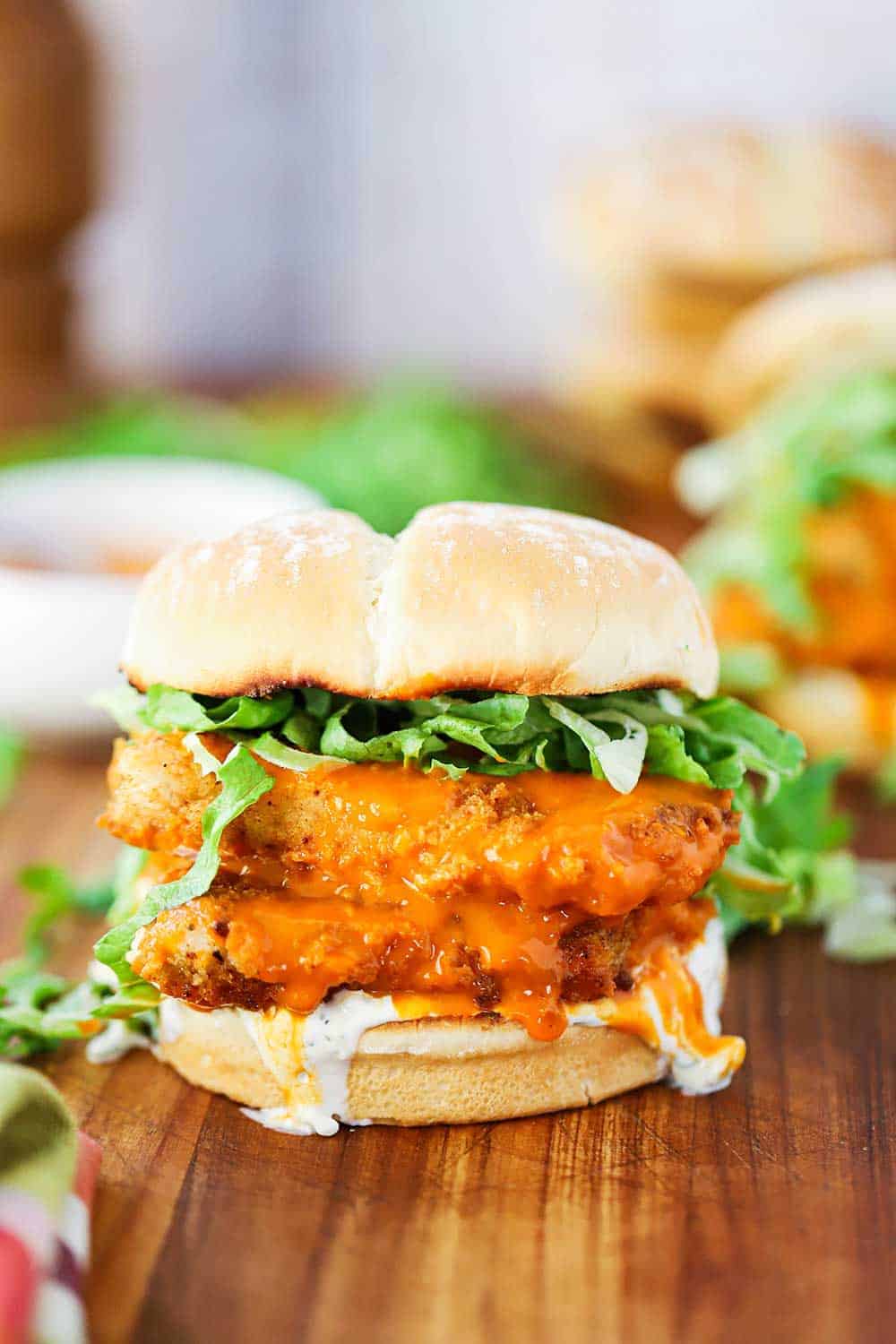 A buffalo chicken sandwich on a wooden board with blue cheese dressing dripping off the side. 