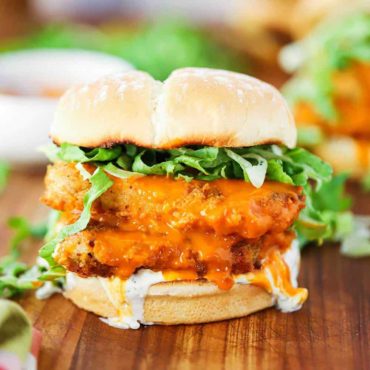 A buffalo chicken sandwich on a wooden board with blue cheese dressing dripping off the side.