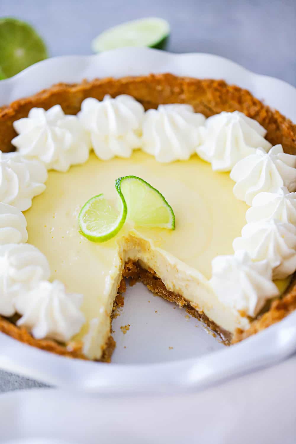 A key lime pie in a white pie dish with a slice cut out of it. 