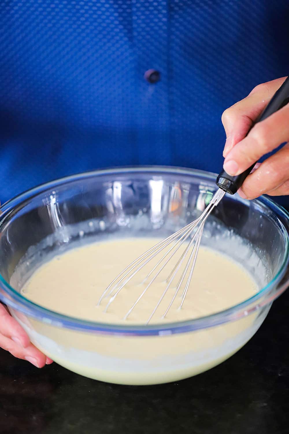 A hand holding a whisk in a glass bowl filled with key lime pie batter. 