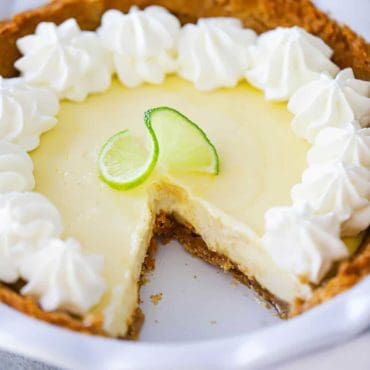 A key lime pie in a white pie dish with a slice cut out of it.