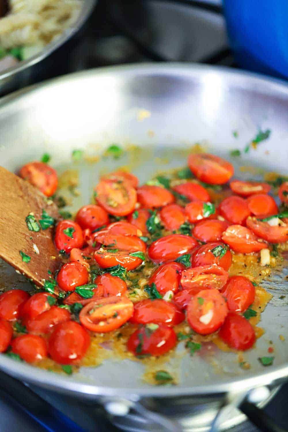 A steel saucepan filled with cherry tomatoes that have been halved and fresh basil.