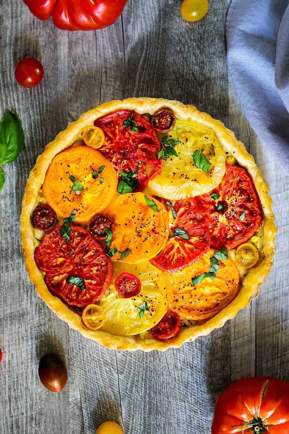 Looking straight down at a tomato tart with corn with fresh tomatoes nearby. 