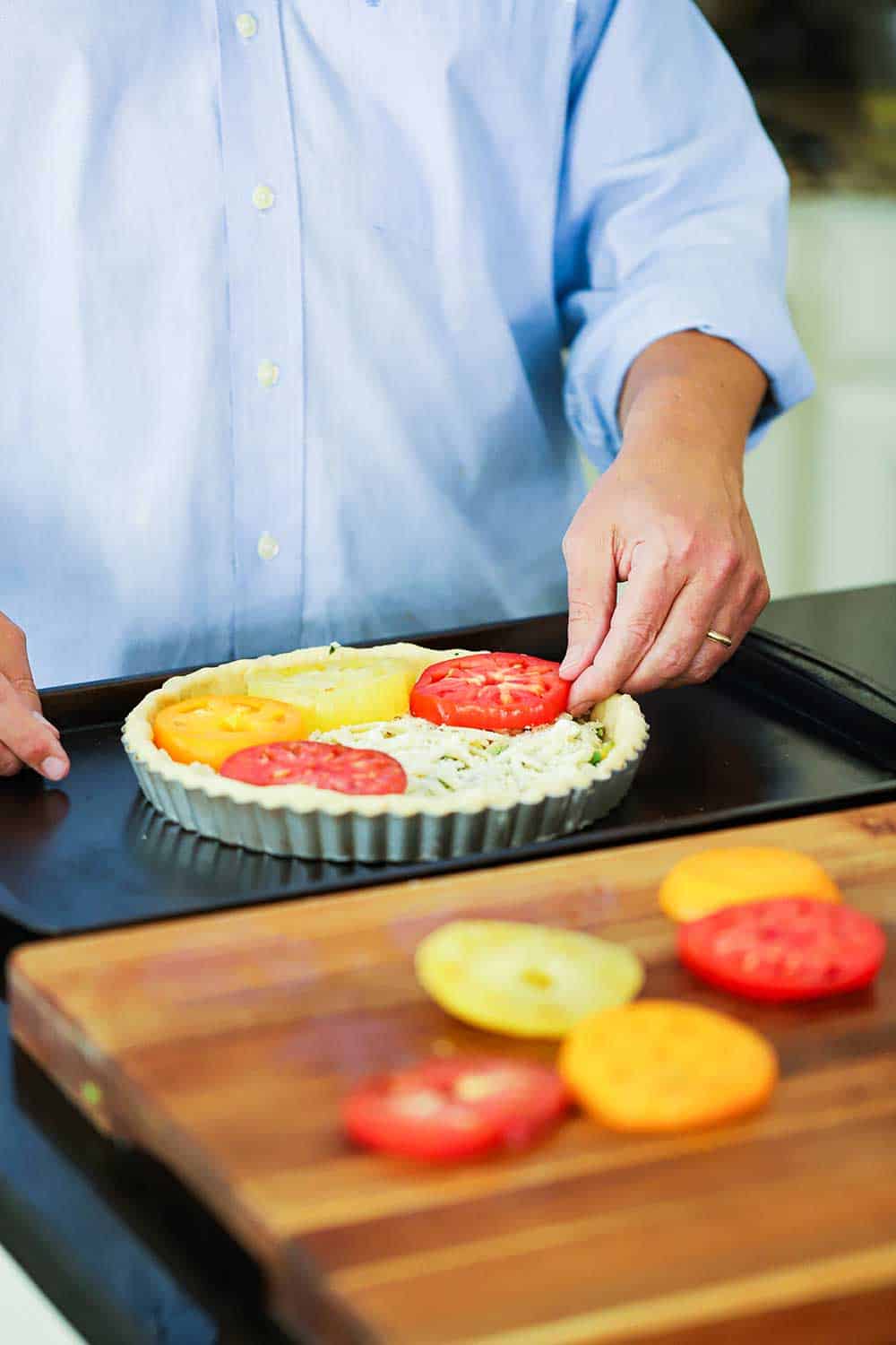 A person layering sliced heirloom tomatoes into a tart pan filled with cheese and corn. 